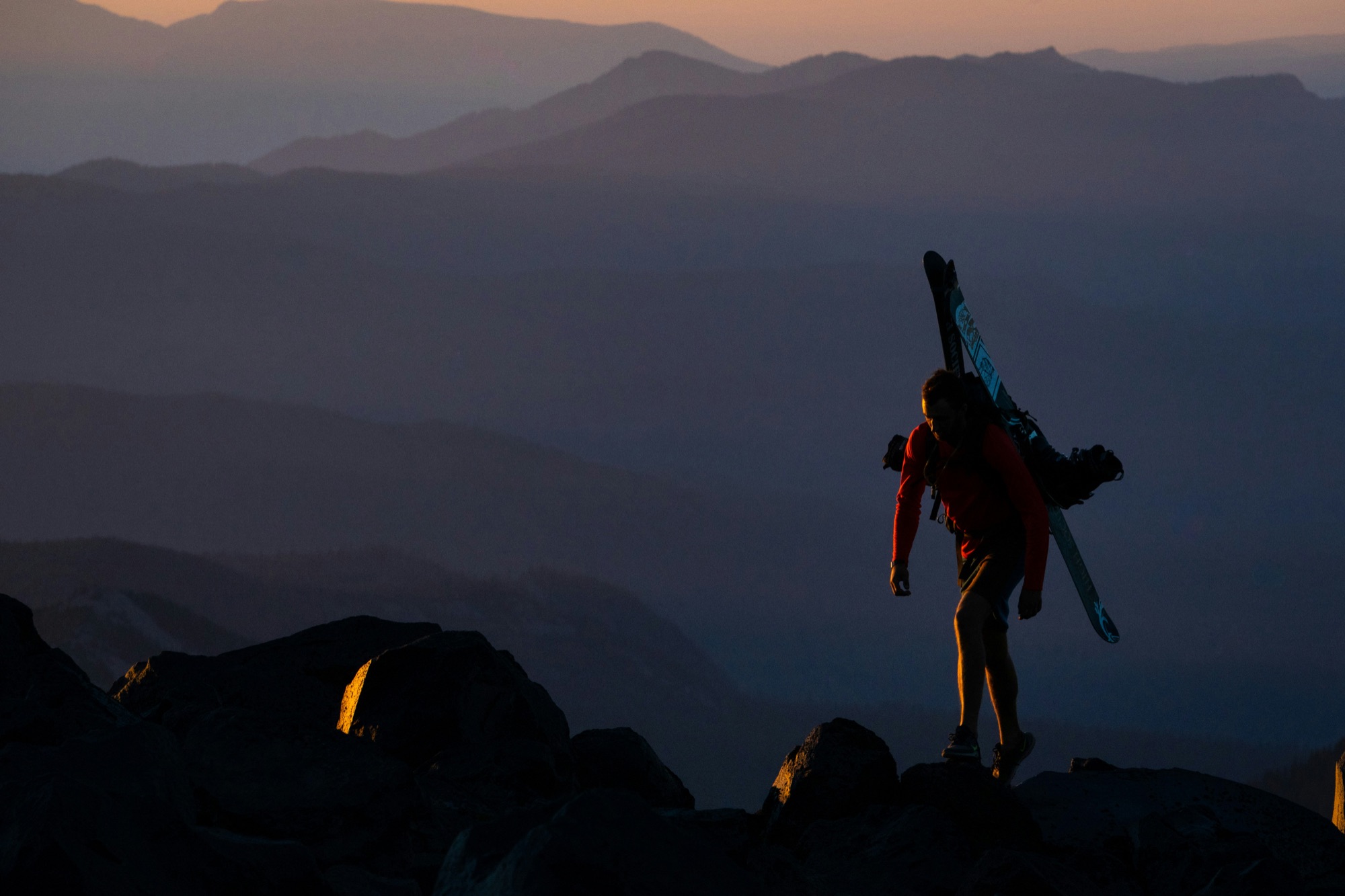 Alpinista em silhueta a caminhar numa crista rochosa ao pôr do sol